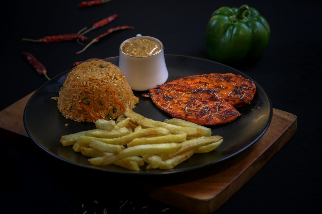 Grilled chicken, rice, fries, and sauce on a dark plate