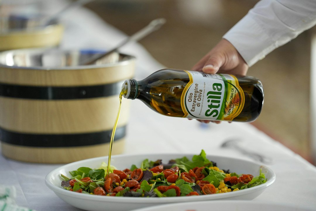 Hand pouring olive oil onto a fresh salad