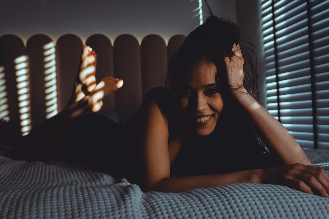 Smiling woman lying on bed with striped light